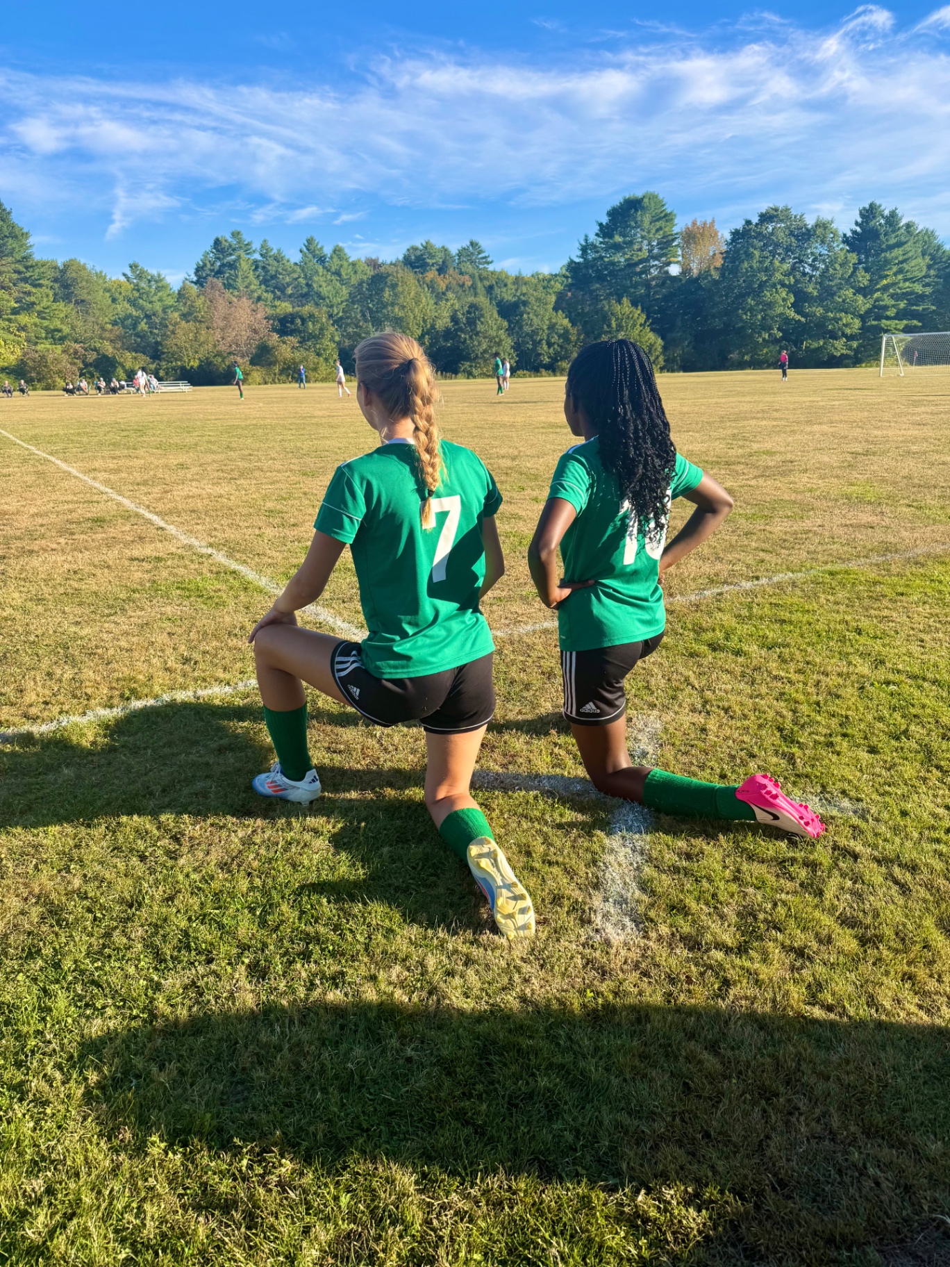 Two Pine Tree Academy players in green jerseys kneeling on the sideline watching the match