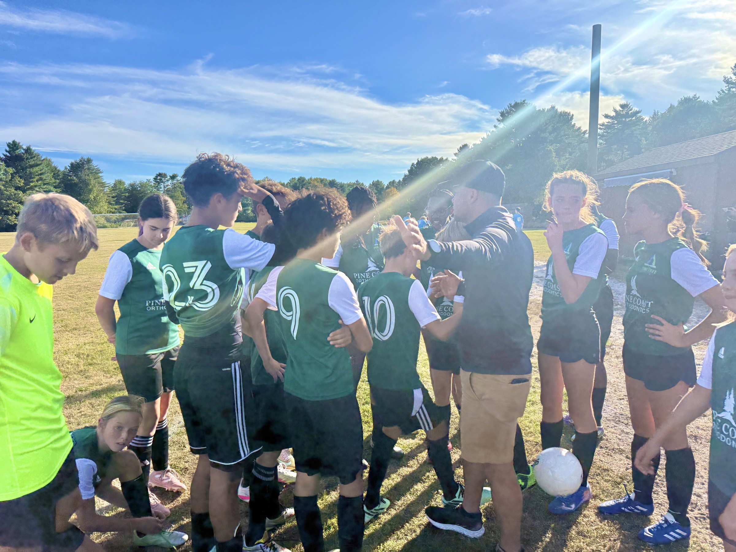 Pine Tree Academy middle school soccer players in green Breakers uniforms huddled together with their coach on the field before the 7-2 home win over Pen Bay Christian School