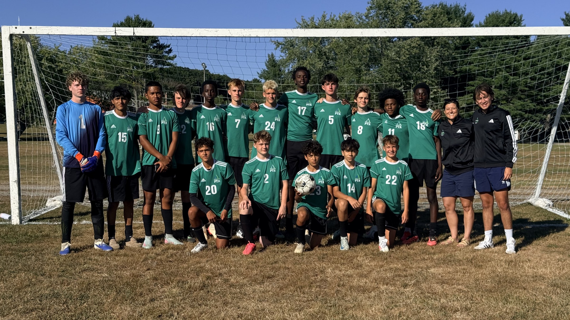Pine Tree Academy boys varsity soccer players and coaches posing together in green uniforms in front of the goal