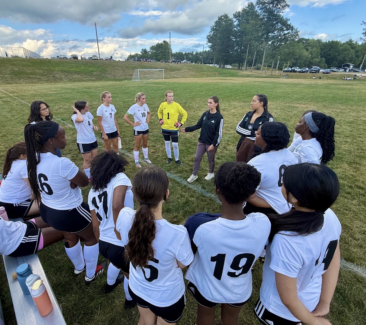 Pine Tree Academy girls varsity soccer team huddled around their coach on the field at Lisbon High School