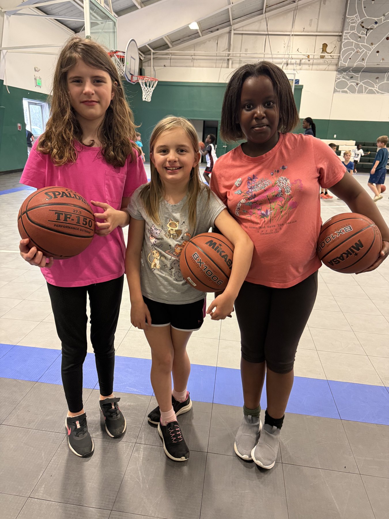 Three young Pine Tree Academy Littles basketball players holding basketballs in the school gym
