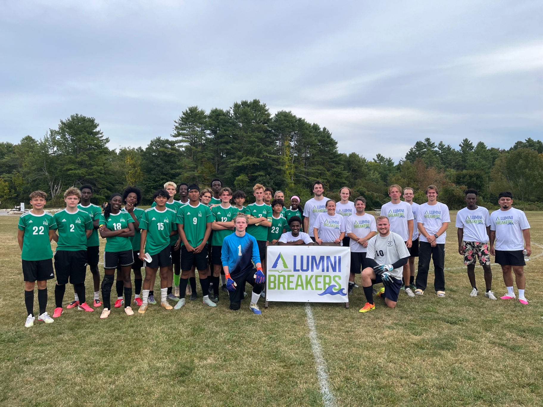 Current Breakers players and alumni posing together with an Alumni Breakers banner after the Alumni Weekend soccer match