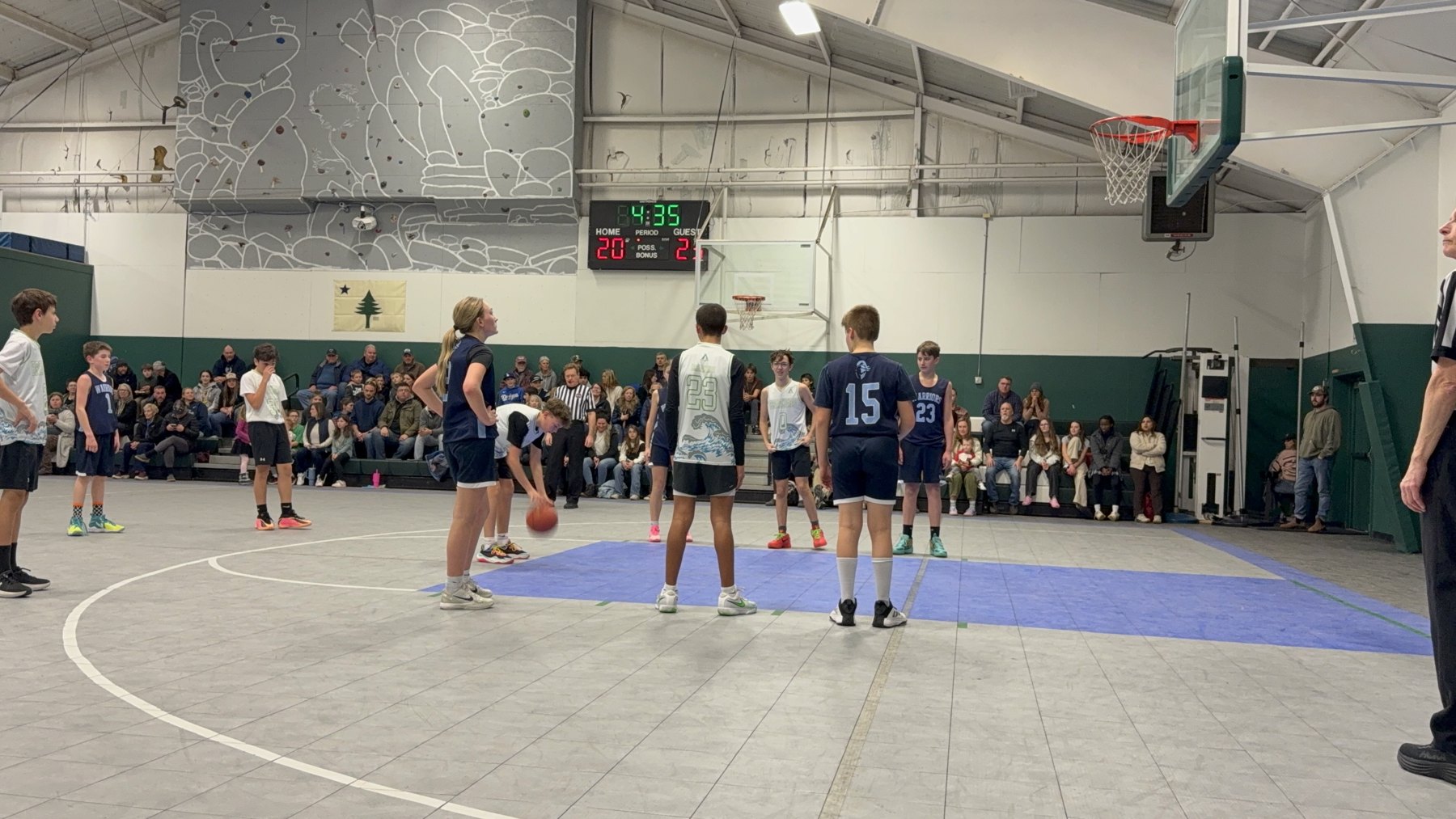 Pine Tree Academy grades 7-8 basketball players bringing the ball up the floor in front of a full gym