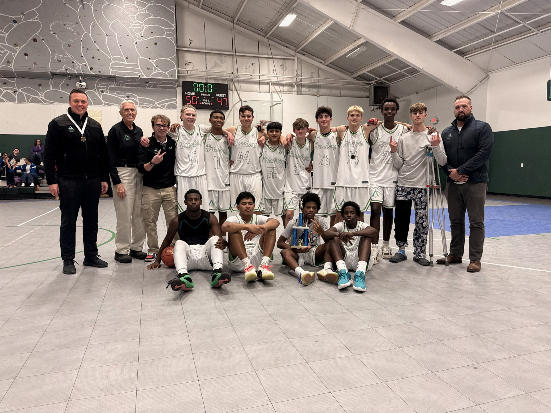 Pine Tree Academy boys varsity basketball team and coaches posed with a trophy in the school gym after a 50-47 win