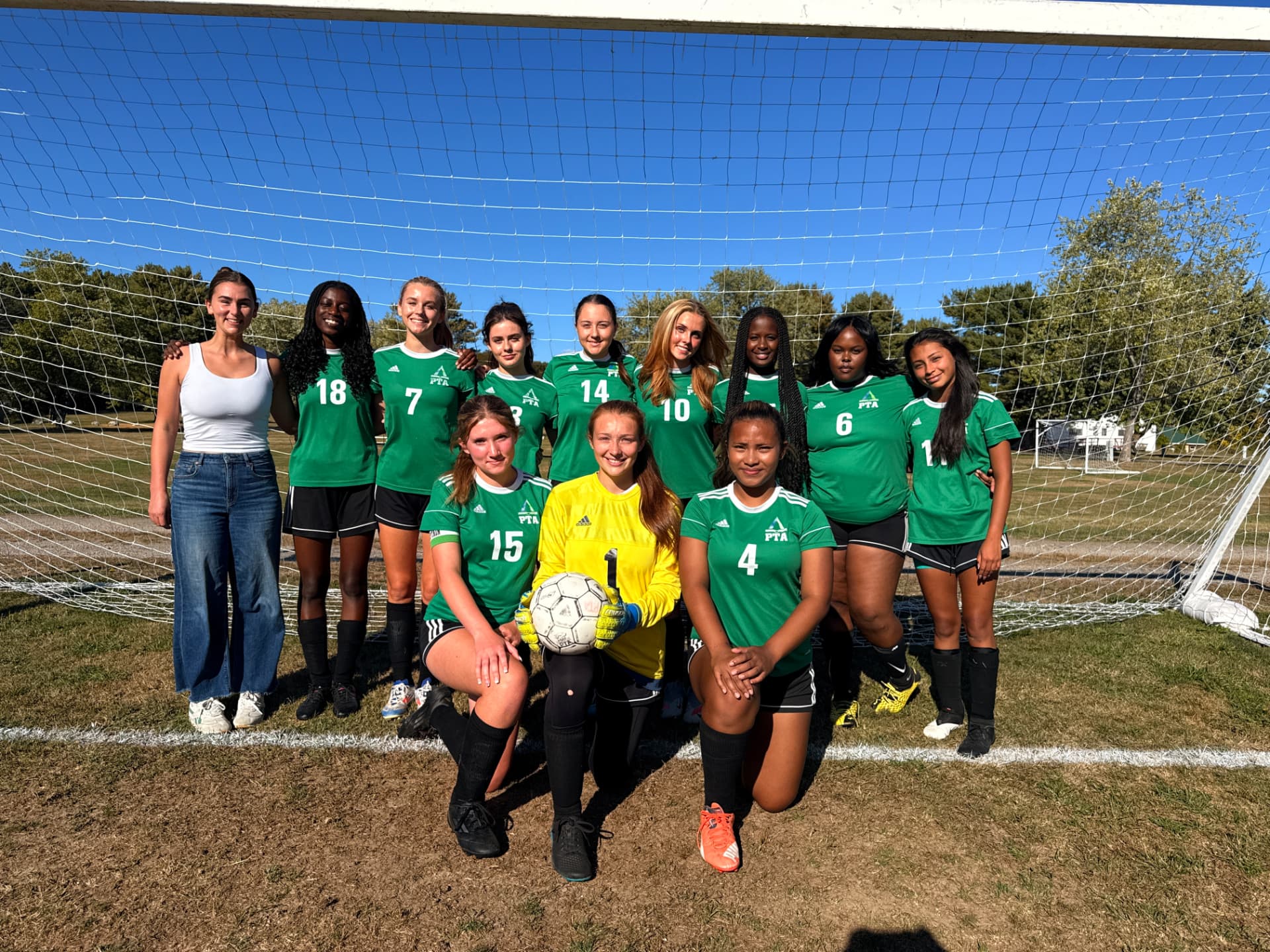 Pine Tree Academy girls varsity soccer team posed in front of the goal in green jerseys on a sunny fall day