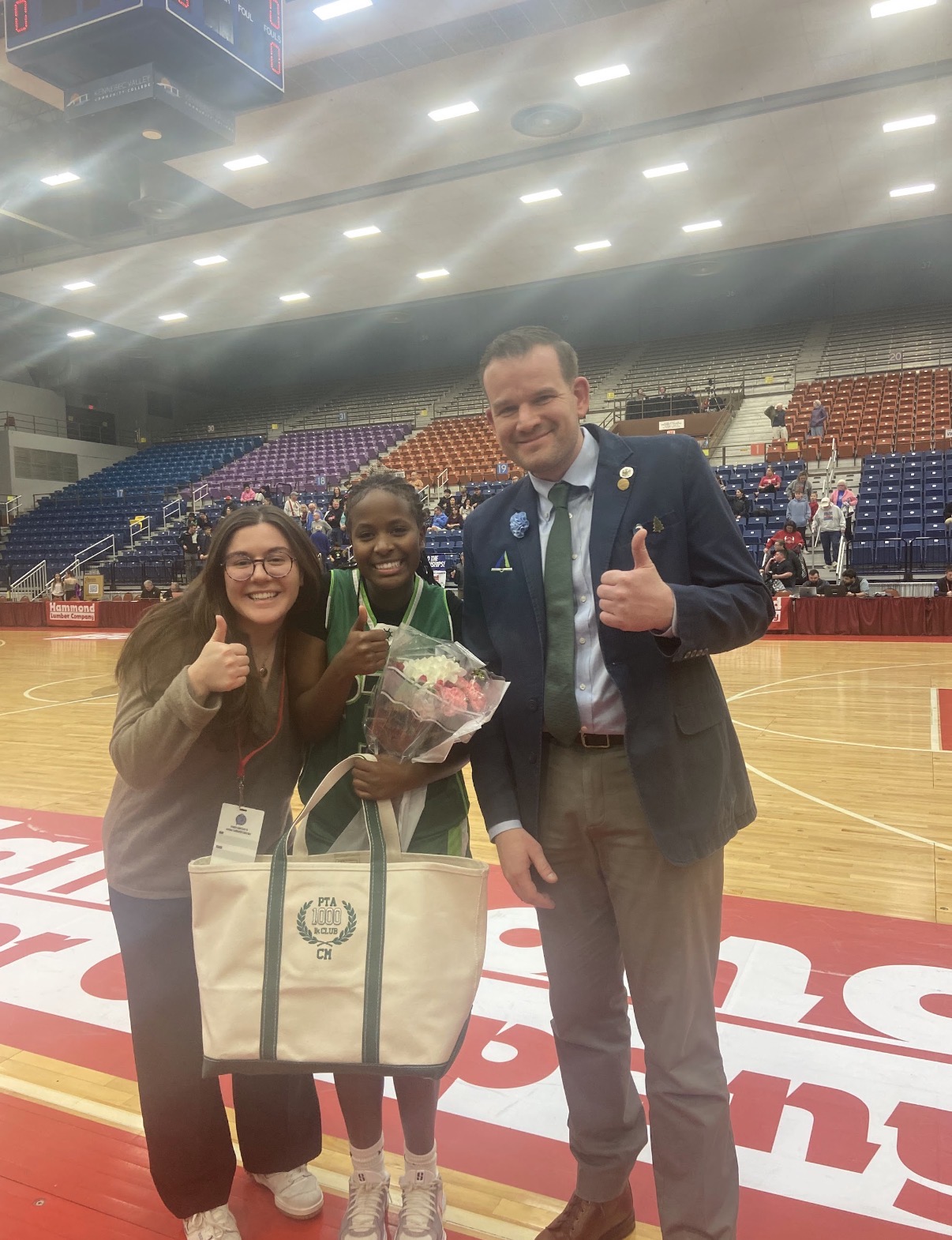 Chantal Mbonimpa holding her PTA 1,000-point club award and flowers at the Augusta Civic Center with two Pine Tree Academy coaches