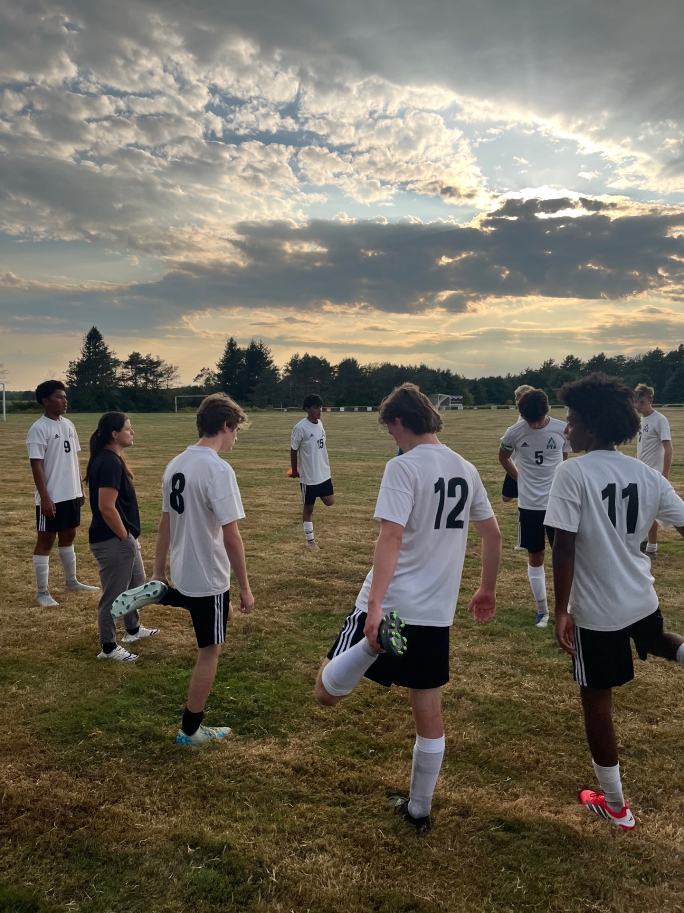 Pine Tree Academy boys varsity soccer players stretching with their coach at sunset before the scrimmage at Richmond