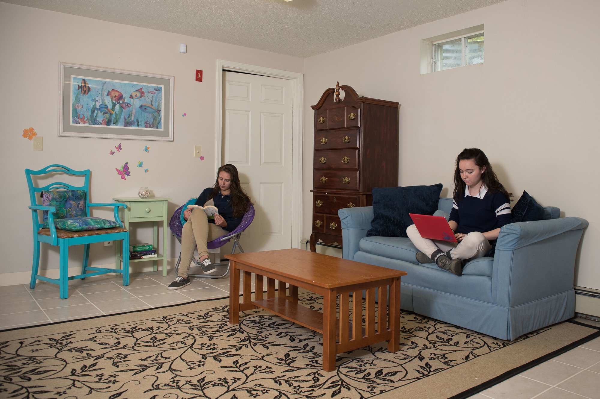 Two Pine Tree Academy boarding students studying and reading in a dorm common room with a sofa, coffee table, and rug