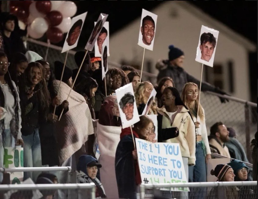 Pine Tree Academy students and families in the stands at the boys soccer regional final holding large player-face signs and a hand-lettered support sign