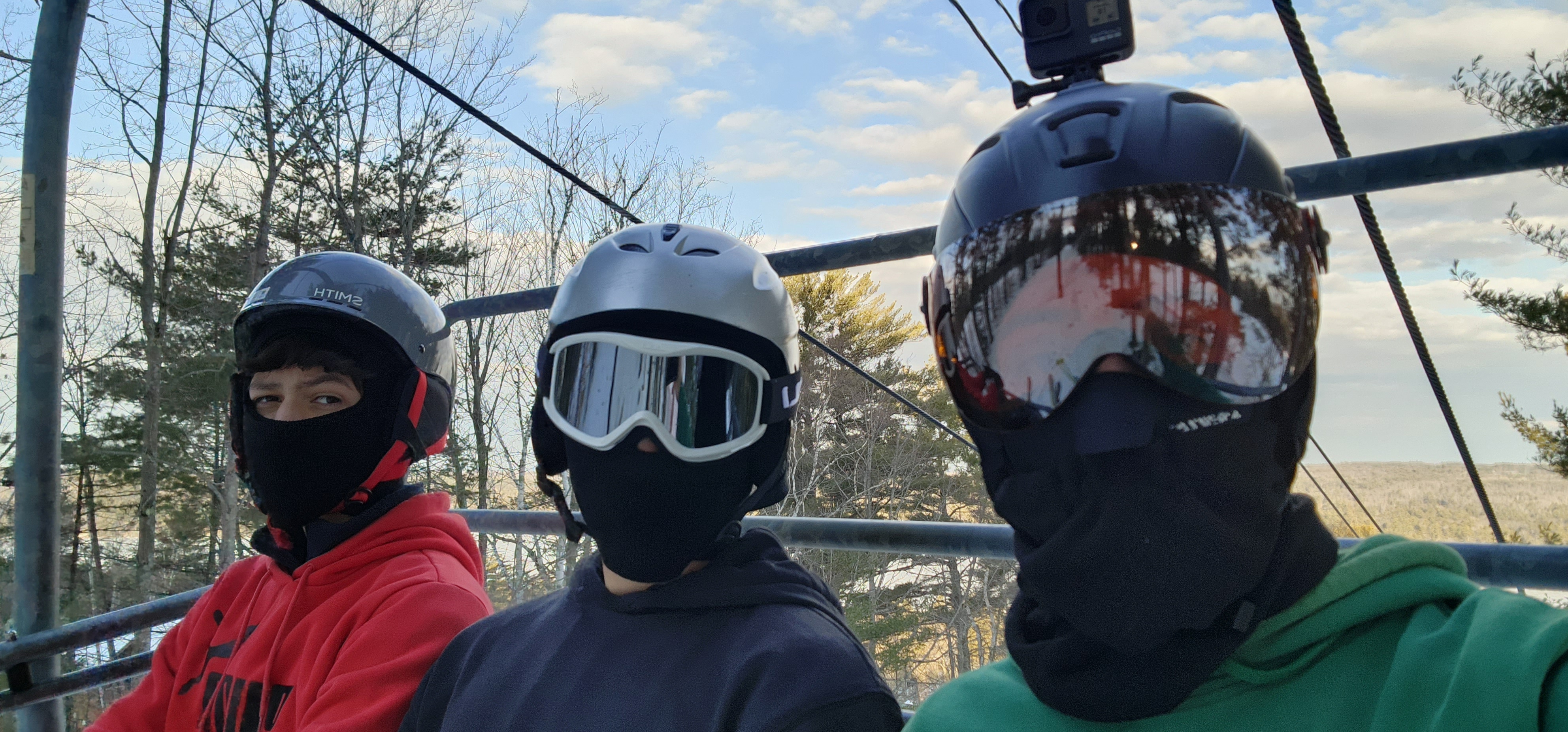 Three helmeted PTA Snowsports participants riding a chairlift