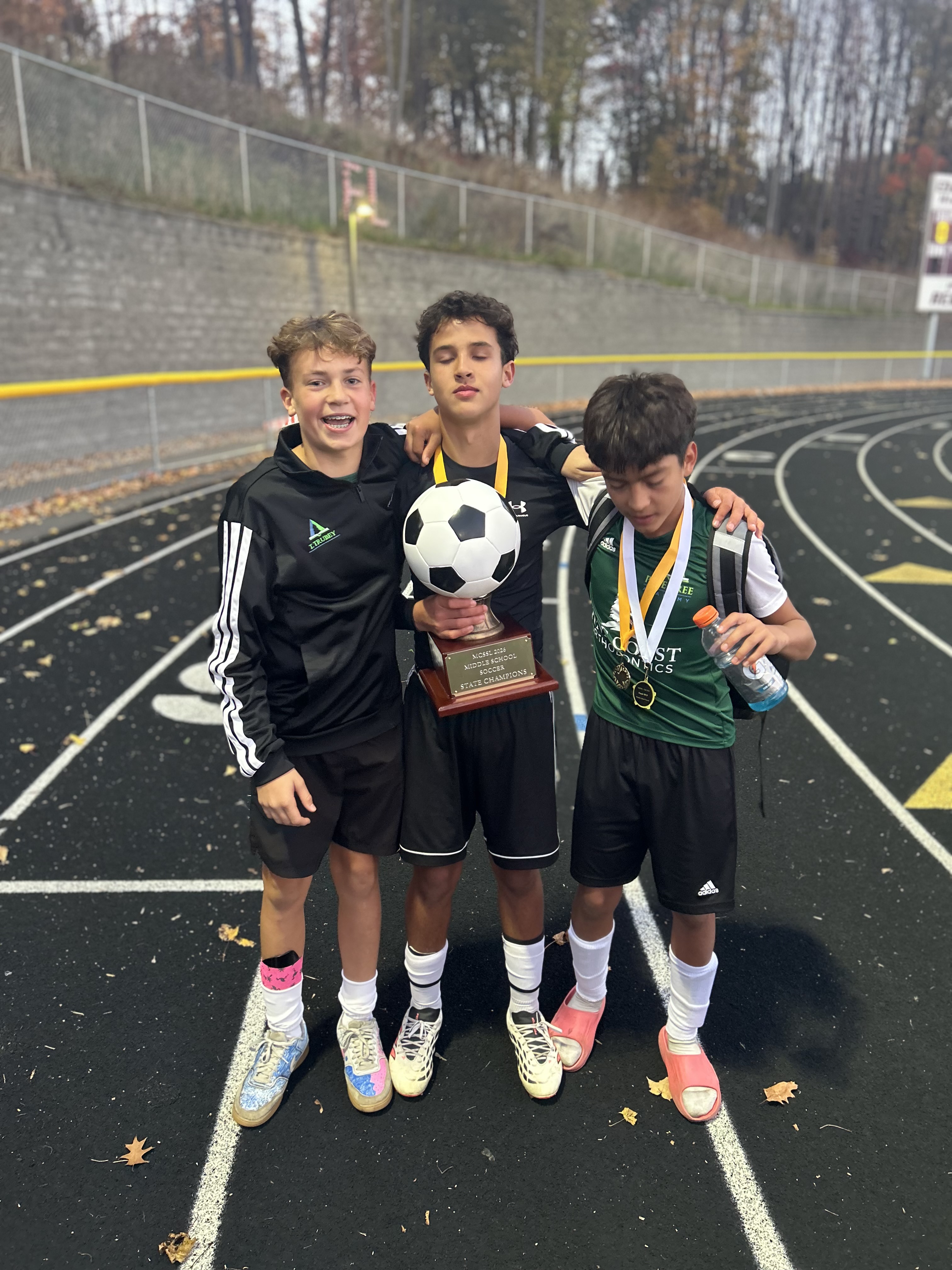 Three Pine Tree Academy students wearing gold medals with the championship trophy held by the central student.